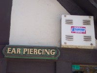 a sign stating 'ear piercing' next to an alarm box