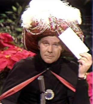 Carnac the Magnificent holding an envelope to his head